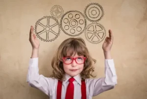 Child in red glasses and tie raising arms with illustrated gears above their head.