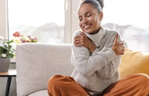 Smiling woman sitting on a couch hugging herself.