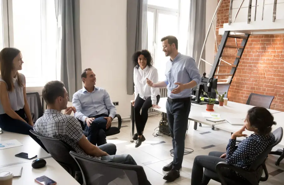 Team gathered in an office with one person standing and speaking to the group.